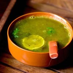 there is a bowl of soup with lemons on the side and green liquid in it