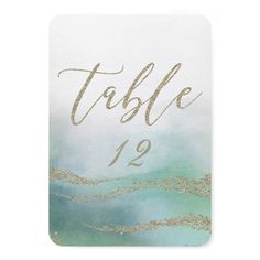 a table number card with gold glitter on the front and green watercolors in the back