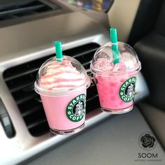 two starbucks drinks sitting on the dashboard of a car with pink and green liquid in them