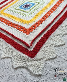 a crocheted blanket is laying on top of a doily and has an orange, yellow, green, blue, red, and white design