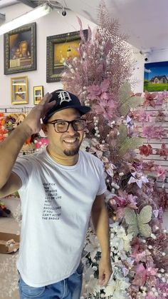 a man standing next to a pink tree in a room with pictures on the wall