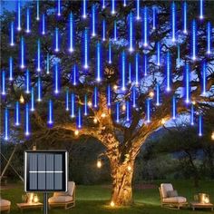 a tree with blue lights hanging from it's branches and some chairs around it