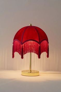 a red table lamp with fringed shades on the top and bottom, sitting on a white surface