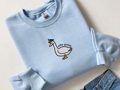 This embroidered Pilot Hat Silly Goose sweatshirt is super soft and cozy. Perfect to lounge around, run errands, or walk your dog. Our crewnecks use the highest quality material for ultra-soft and comfortable wear, with advanced embroidery to ensure vibrant colors and detailed graphics. Product Details:✨ * 50% cotton, 50% polyester * Pre-shrunk * Classic fit * 1x1 athletic rib knit collar with spandex * Air-jet spun yarn with a soft feel and reduced pilling * Double-needle stitched collar, shoulders, armholes, cuffs, and hem Sizing👚 All sweatshirts come in multiple colors and 5 different sizes, ranging from Small to XX-Large. This unisex crewneck sweatshirt is intended to be loose/oversized for women to give a chic and laid-back vibe. If you want something more fitted, we recommend orderi Casual Embroidered T-shirt For Loungewear, Casual Embroidered Loungewear T-shirt, Casual Loungewear Tops With Custom Embroidery, Goose Sweatshirt, Pilot Hat, Advanced Embroidery, Fabric Pilling, Silly Goose, Embroidered Crewneck