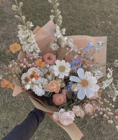 a person holding a bouquet of flowers in their hand on the ground with grass behind them