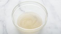 a clear glass filled with liquid sitting on top of a white marble countertop next to an orange slice