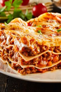 a white plate topped with lasagna covered in sauce and cheese next to vegetables