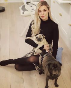 a woman sitting on the floor with two pugs in her lap and one standing up