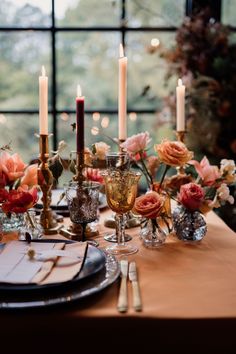 a table set with candles, flowers and plates for an elegant dinner or party in front of a large window