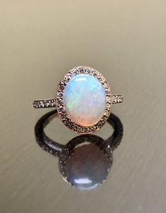 DeKara Designs Collection Our latest design! An elegant and lustrous Opal cabochon surrounded by beautiful diamonds in a halo setting. Metal- 14K Rose Gold, .583. Size- 4-12 Stones- Center Features a Oval Fiery Opal Cabochon Cut 2.60-2.90 Carats, 11.10 MM Long, 9 MM Wide, 44 Round Diamonds, F Color VVS Clarity, 0.35 Carats. Latest of my creations. A beautiful Opal Halo Diamond Ring. The Opal is professionally prong set in between 4 double prongs. There are 10 pave set round diamonds on each side Luxury Oval Opal Ring With Halo Setting, Luxury Rose Gold Opal Ring, Elegant Opal Ring With Oval Cabochon And Accent Stones, Elegant Oval Cabochon Opal Ring With Accent Stones, Diamond Opal Cabochon Ring For Anniversary, Diamond Cabochon Opal Ring For Anniversary, Anniversary Diamond Opal Cabochon Ring, Elegant Cabochon Opal Ring For Wedding, Formal Rose Gold Opal Ring With Diamond