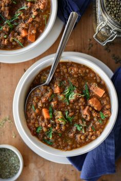 two bowls filled with lentula and carrots on top of a wooden table next to a spoon