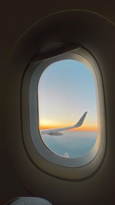 an airplane window looking out at the ocean and sunset from it's plane wing