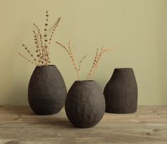 three black vases sitting on top of a wooden table next to each other with plants in them