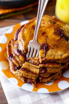 a stack of pancakes with syrup on top and a fork stuck in the middle, sitting on a polka dot plate