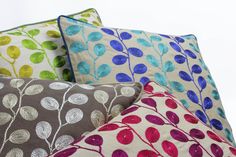 four different colored pillows stacked on top of each other, one with green and blue leaves