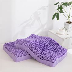 two purple pillows sitting next to each other on a white table with a potted plant in the background