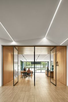 an empty room with wooden floors and sliding glass doors leading to the dining area is lit by recessed lights