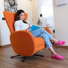 a woman sitting in an orange chair reading a book while wearing bright pink slippers