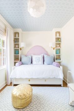 a white bed sitting in a bedroom next to a window with blue and white curtains