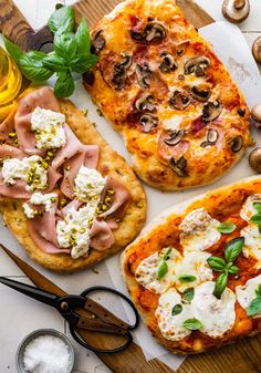 three different types of pizza on a cutting board next to some scissors and other food items