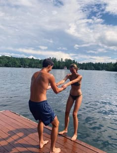 a man and woman standing on a dock next to the water holding hands with each other