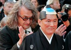 an older man in a black kimono is surrounded by photographers as he walks down the red carpet