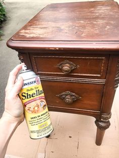 a person holding a spray paint next to a brown wooden table with drawers on it