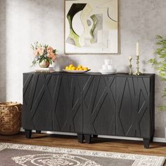 a sideboard with fruit and flowers on it in front of a wall mounted painting