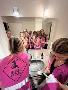 a group of women in pink vests standing around a bathroom sink