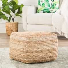 a living room area with a white couch and green plants on the floor, along with a round woven ottoman