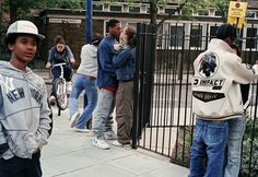 a group of young men standing next to each other on a sidewalk near a fence