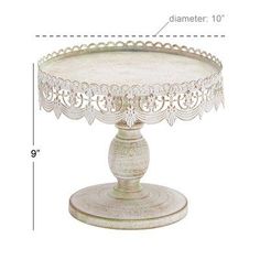 a white cake stand with an ornate design on the top and bottom, sitting on a table