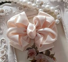 a close up of a pink bow on a white frame with flowers and pearls around it