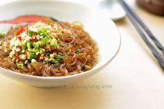 a white bowl filled with noodles and vegetables next to chopsticks on a table