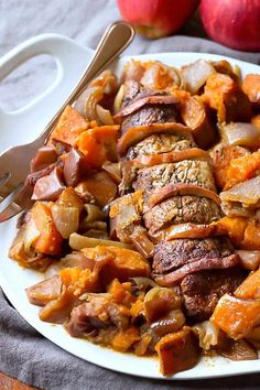 a white plate topped with meat and veggies next to two apples on a table