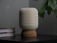 a white vase sitting on top of a wooden table next to a book and plant