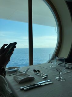 a person sitting at a table with a cell phone in front of a window overlooking the ocean