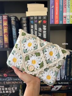 a hand holding up a crocheted purse in front of a bookshelf