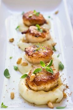 four scallops on top of mashed potatoes and garnished with green leaves