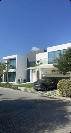 a black car parked in front of a large white house with palm trees and bushes