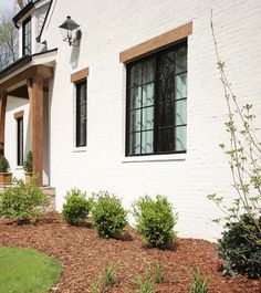 a white brick house with black windows and bushes