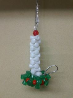 a white beaded christmas decoration hanging from a silver chain on a table with red and green beads