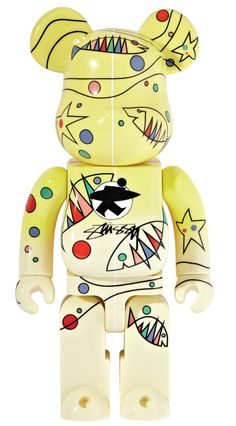 a yellow bear toy with colorful designs on it's face and chest, sitting in front of a white background