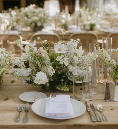 the table is set with white flowers and silverware