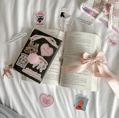 an open book sitting on top of a bed next to a pink bow and some stickers