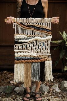 a woman standing in front of a wall hanging with different types of yarn on it