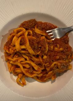 a white plate topped with pasta covered in sauce and meat next to a silver fork