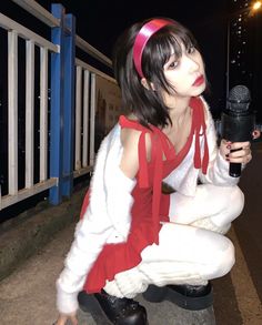 a woman dressed in white and red holding a microphone while kneeling down on the ground