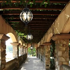 the walkway is lined with stone pillars and lanterns hanging from the pergolated roof