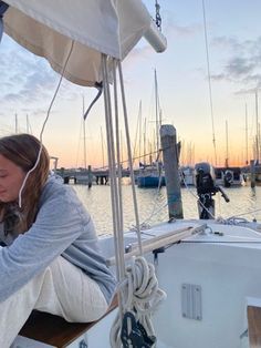 a woman sitting on the deck of a sailboat at sunset, listening to headphones